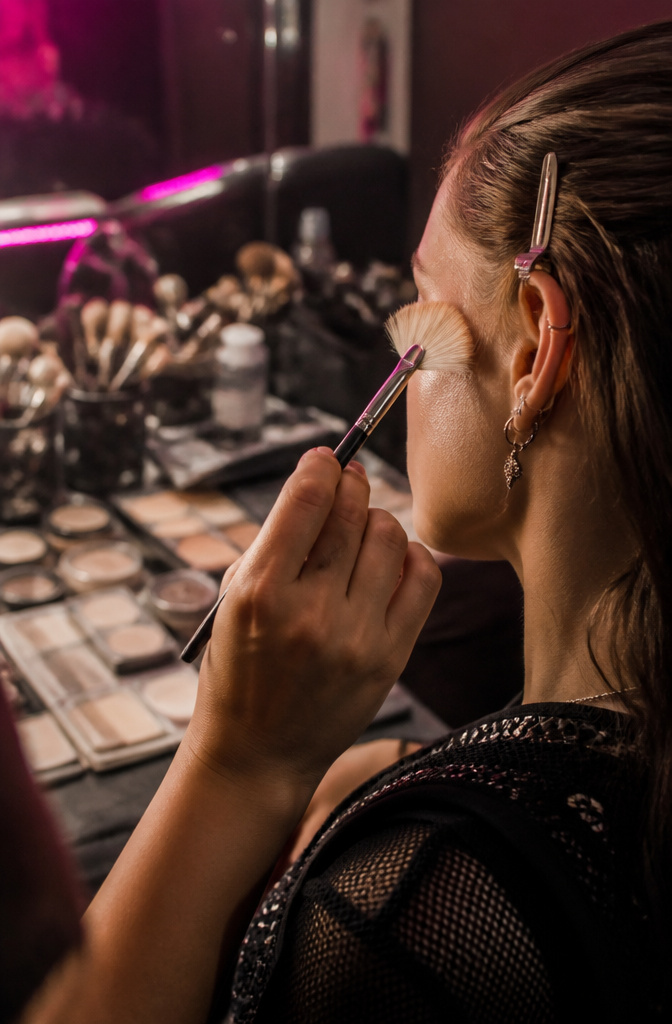 Makeup artist applying pressed powder to a model's cheekbones.