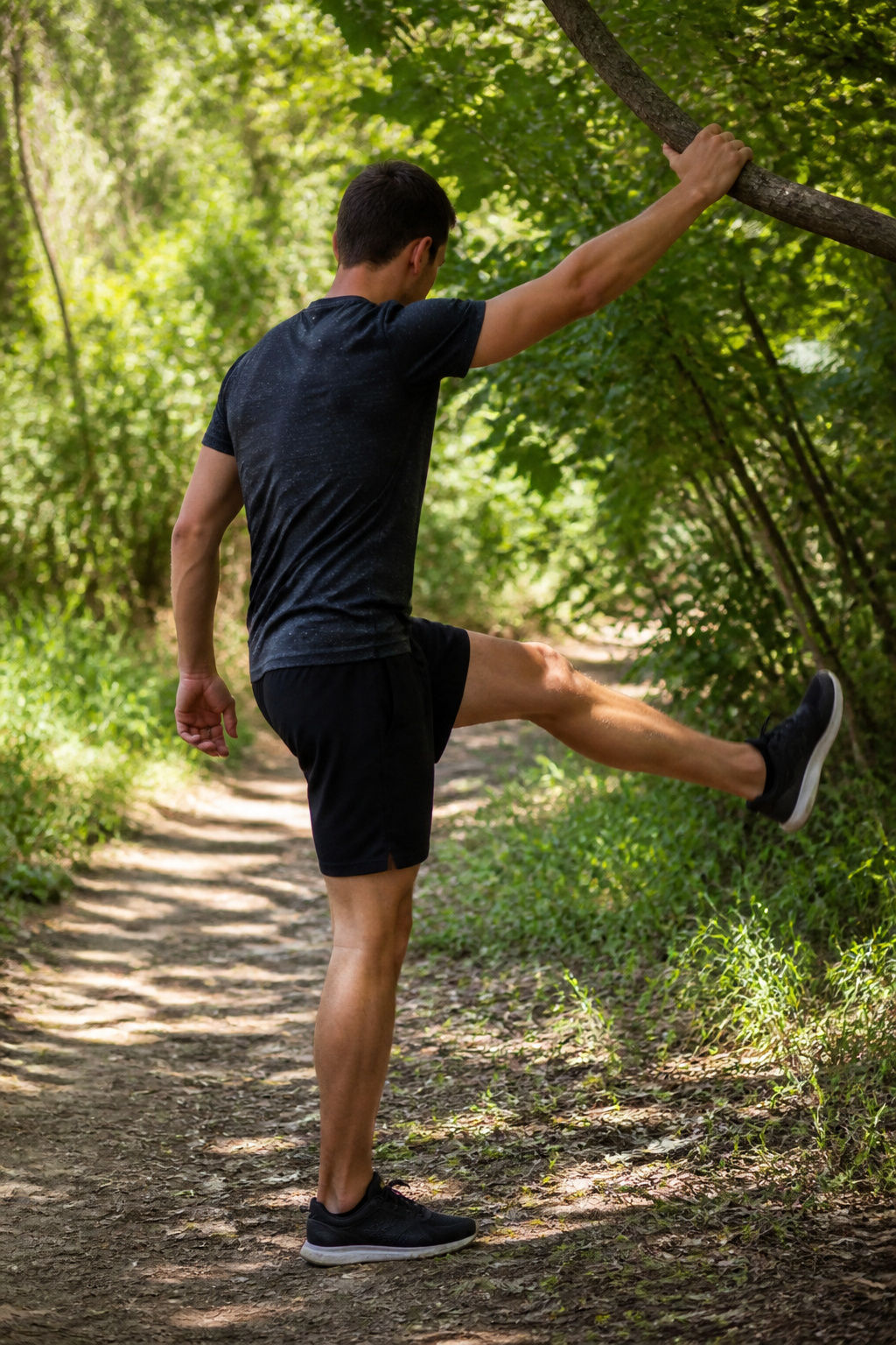 Individual demonstrating controlled leg swings while holding onto a tree branch.