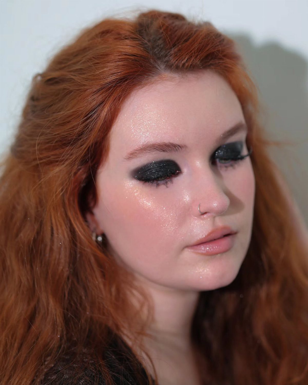Woman with red hair wearing glittery dark eyeshadow and glossy pink lips.