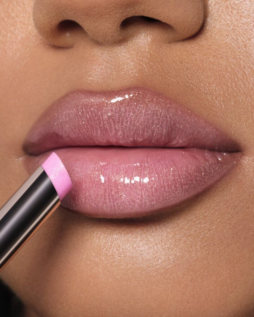 Light pink glossy lips being applied with a lipstick applicator in close-up.