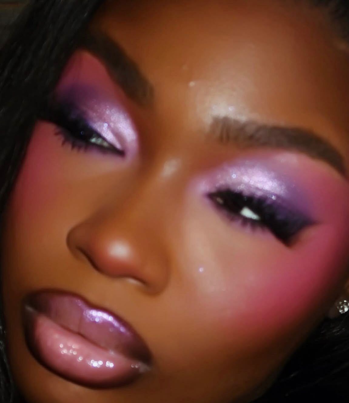 Person with shimmering purple and pink eyeshadow and glossy purple lips.