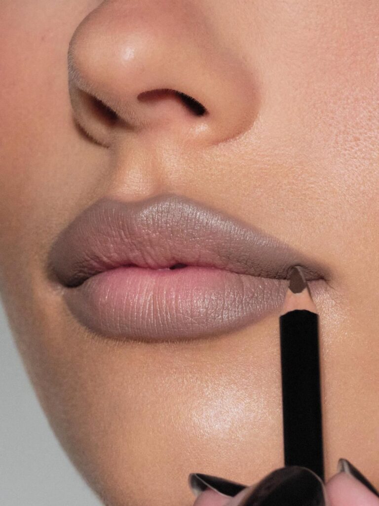Taupe-grey liquid lipstick being applied to a person's lips with a black applicator.