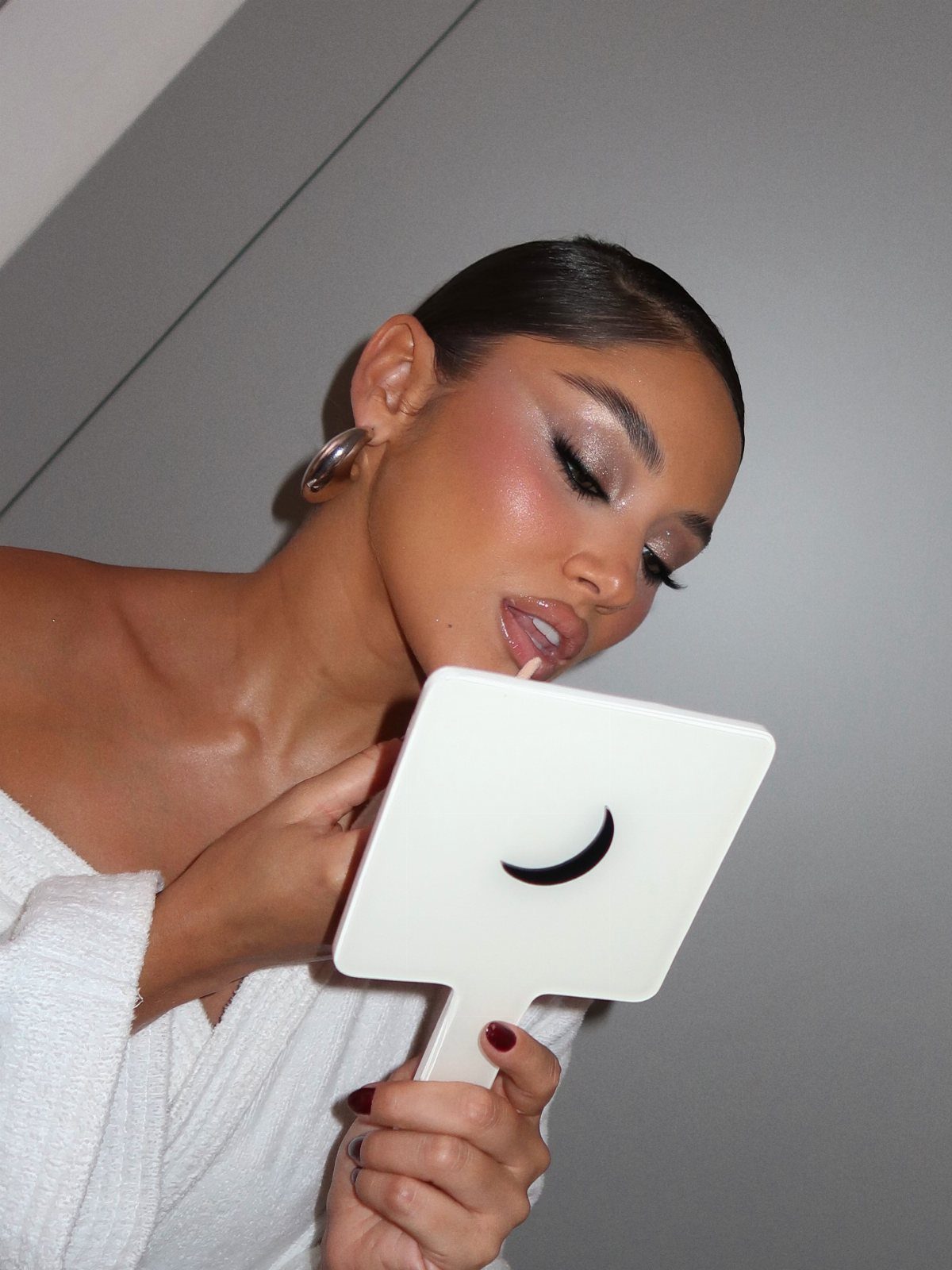 Woman with shimmering foxy glam makeup looking into a white handheld mirror