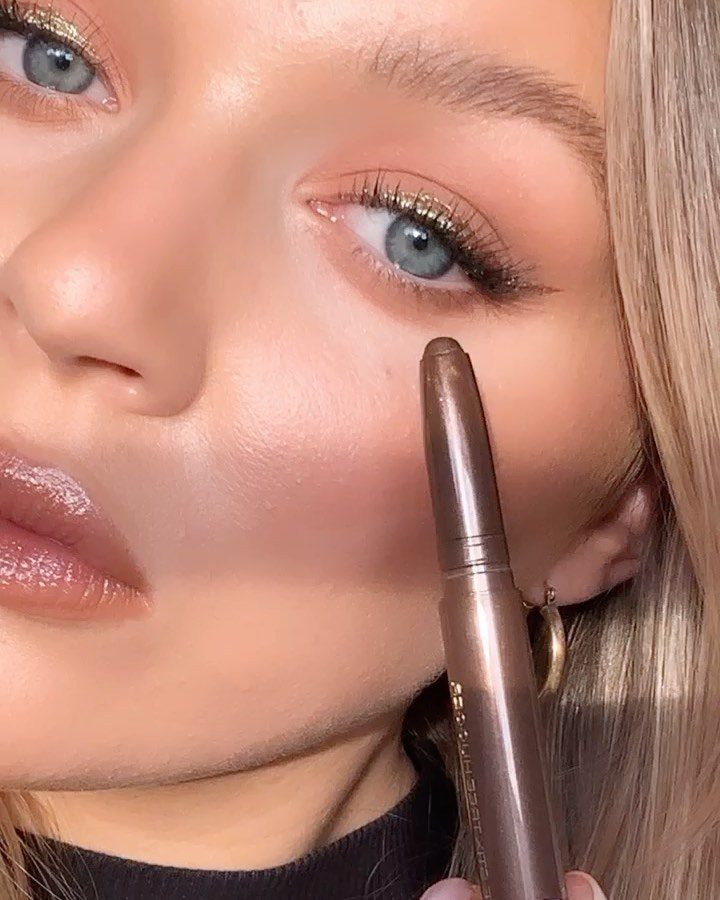 Woman with gold shimmery eyeshadow and glossy lips holding a makeup pencil.