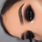 Bold black smokey eye makeup with glitter and defined arched eyebrows.