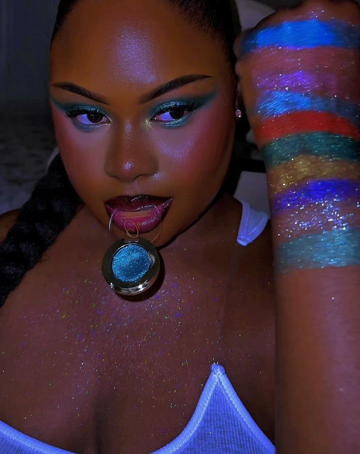 Woman with metallic teal eyeshadow and colorful shimmering eyeshadow swatches on her arm.
