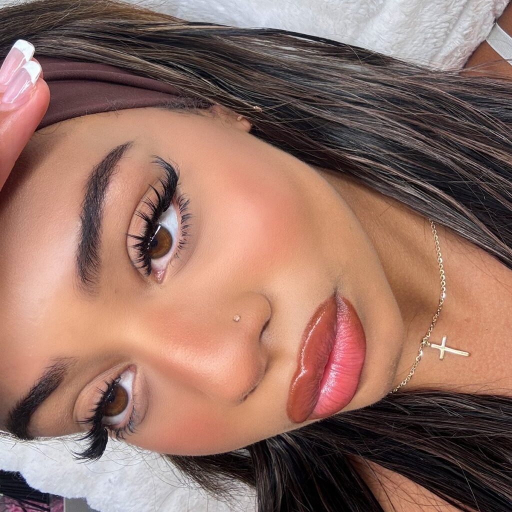 Woman with dramatic curled eyelashes, defined brows, and glossy pink lips posing closely.