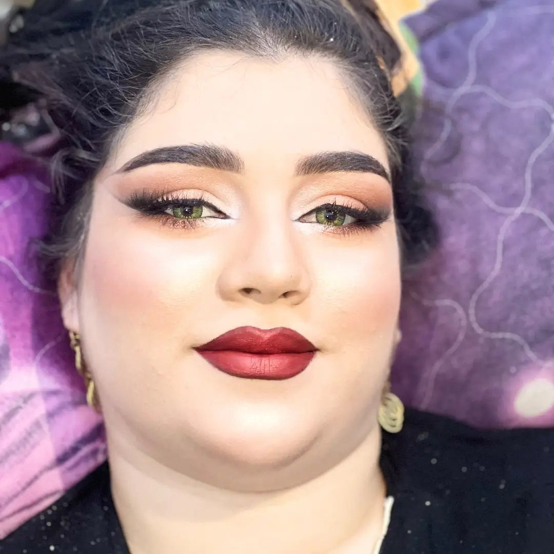 Woman with brown skin wearing bold red lipstick and winged black eyeliner makeup.