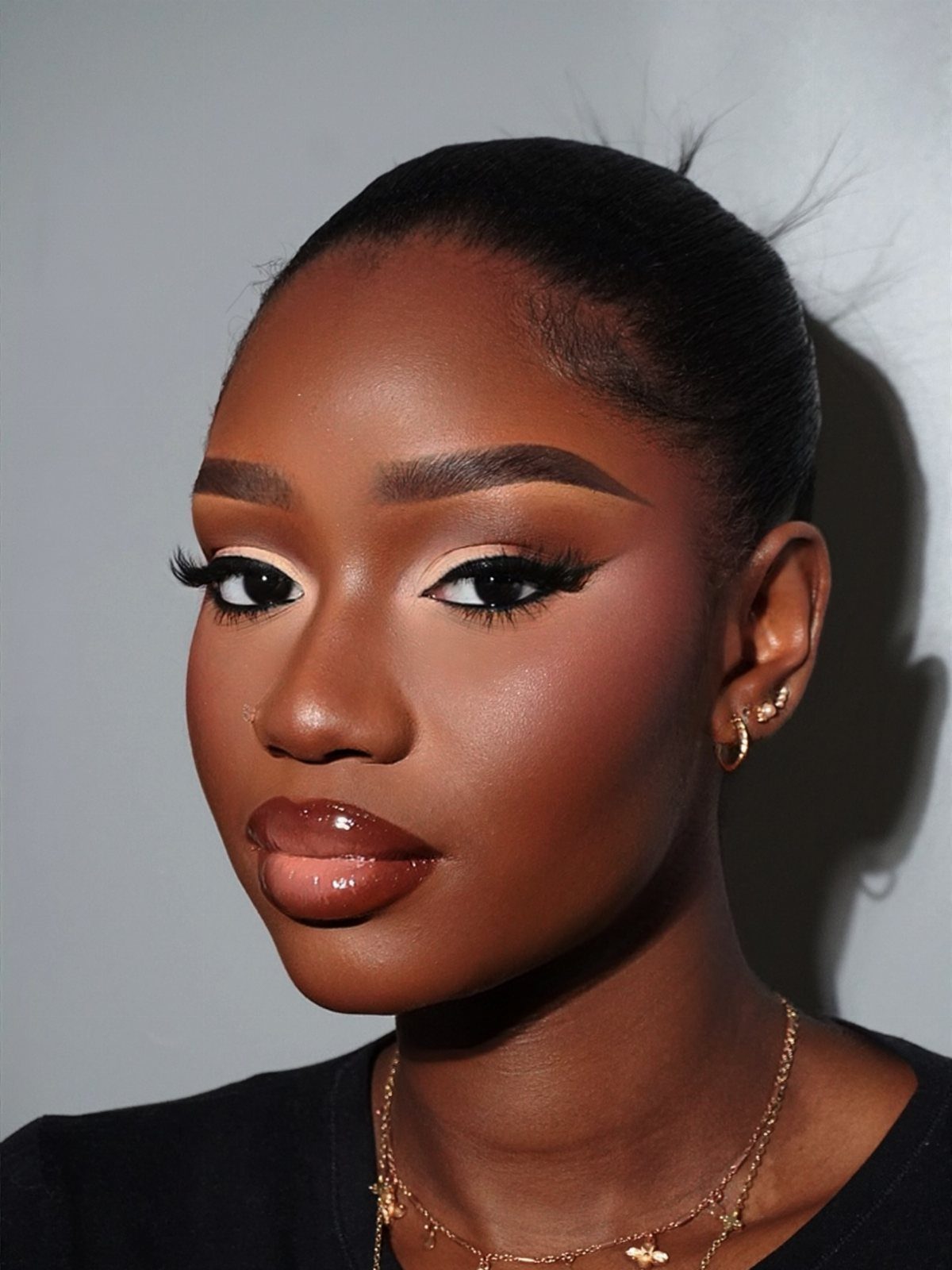 Woman with dark skin wearing winged eyeliner and glossy brown lipstick.