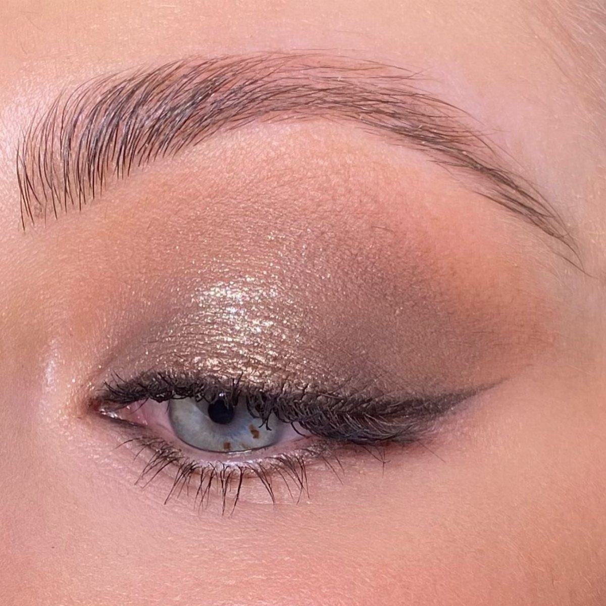 Close-up of an eye with shimmering gold eyeshadow and subtle smokey eyeliner.