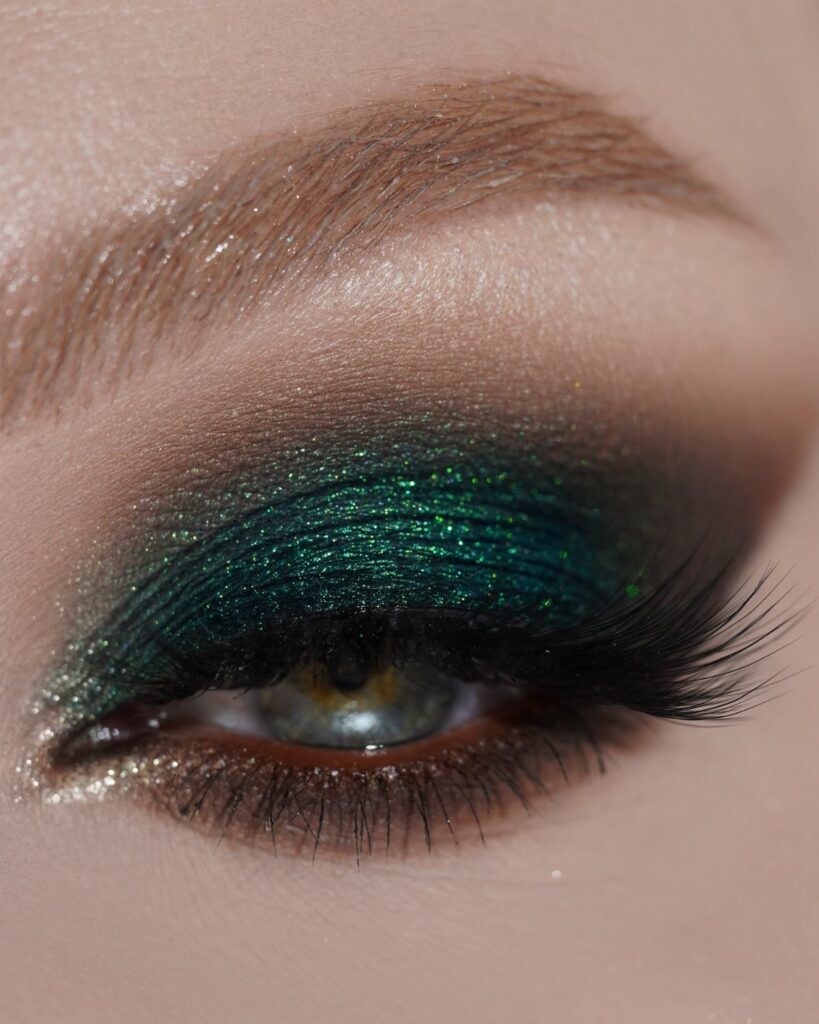 Close-up of an eye with shimmering emerald green smoky eyeshadow and long lashes.