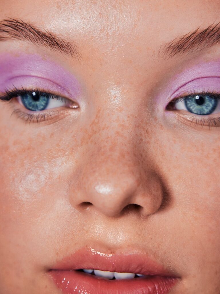 Person with blue eyes wearing light purple eyeshadow and glossy pink lips