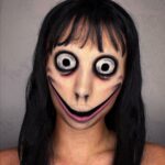 Person with long black hair wearing scary face paint with oversized eyes and wide smile