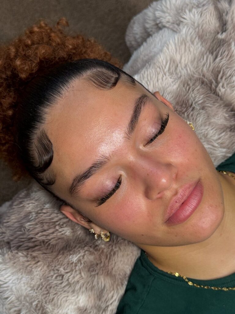 Woman with defined, tinted eyebrows and styled hair lying on a furry pillow.