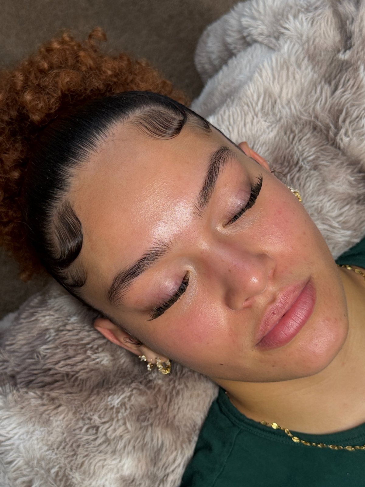 Woman with defined, tinted eyebrows and styled hair lying on a furry pillow.