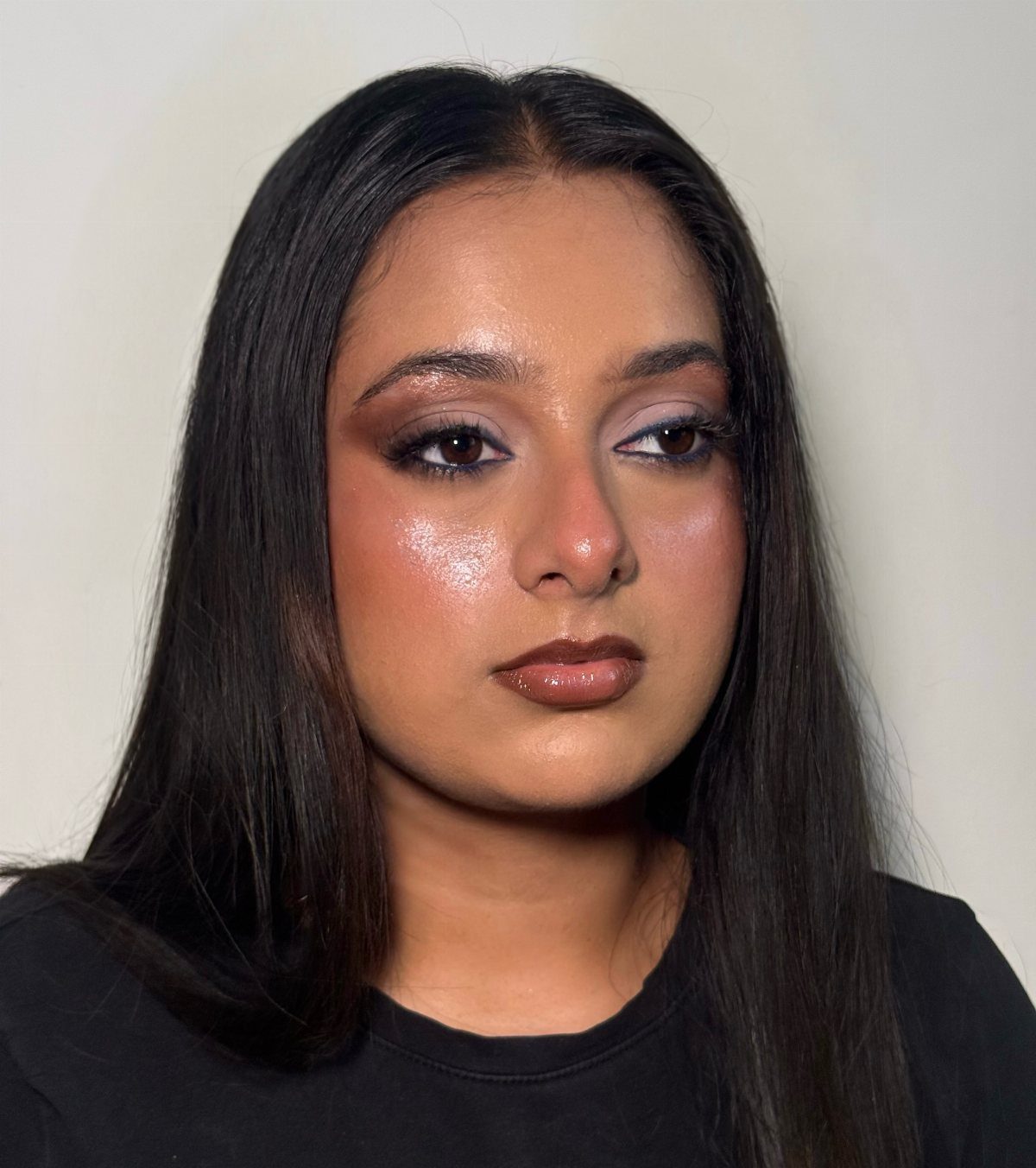 Woman with full beat makeup, shimmering eyeshadow and brown lipstick against grey background