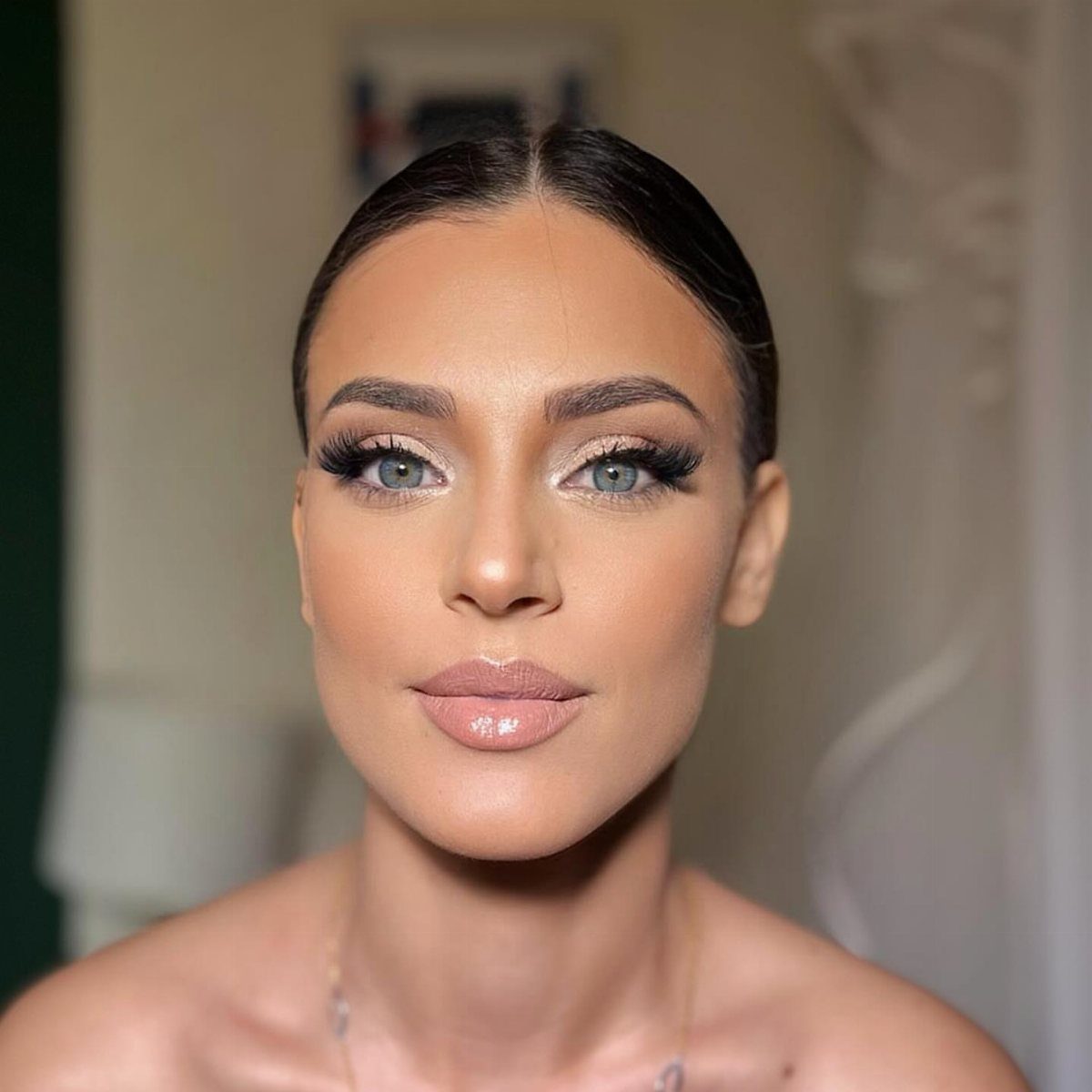 Woman with blue eyes wearing shimmering gold wedding makeup and glossy nude lips.